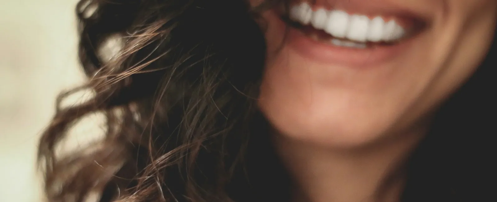 Close-up of woman smiling with healthy white teeth and dark curly hair framing her face.
