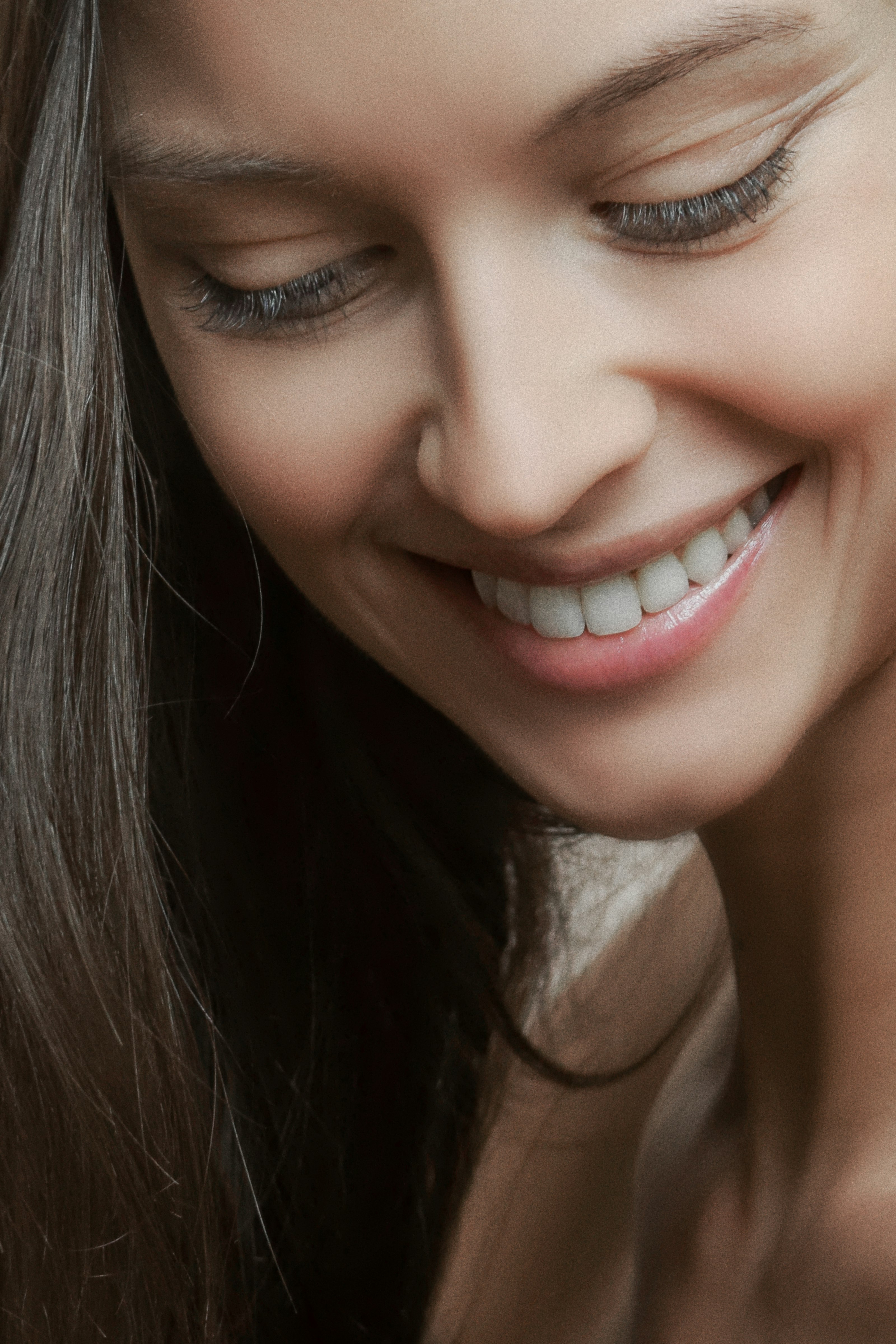 Close-up of a smiling woman with long hair and smooth skin looking downwards showing natural beauty.