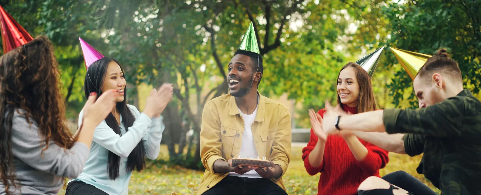 Group of friends wearing party hats enjoying a picnic celebration outdoors on a sunny day