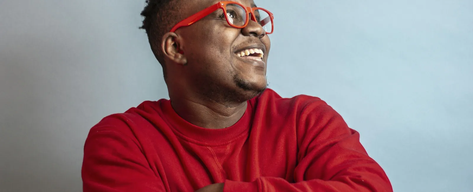 Man wearing red glasses and a red sweatshirt smiling and looking to the side against a plain gray background