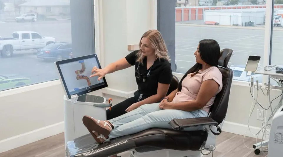 Dentist explaining dental scan results on screen to patient seated in dental chair in modern clinic.