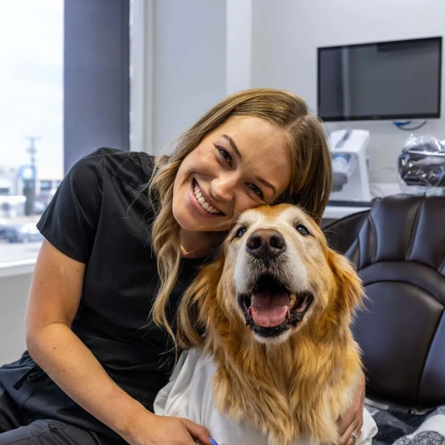 Smiling woman hugging happy golden retriever in a bright room with office furniture and technology.