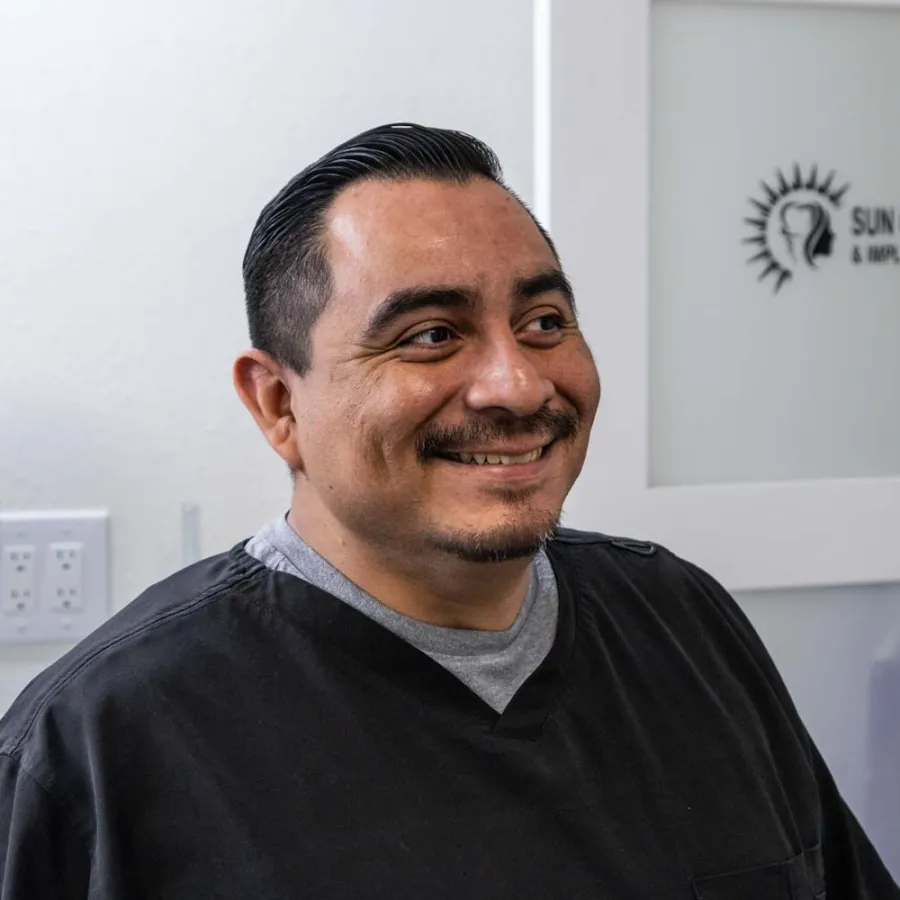 Smiling male dentist in black scrubs inside Sun City Oral Surgery and Implant Center clinic.