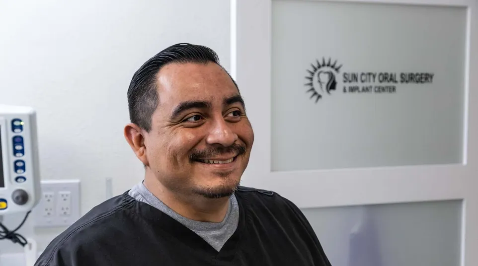 Smiling male dentist in black scrubs inside Sun City Oral Surgery and Implant Center clinic.
