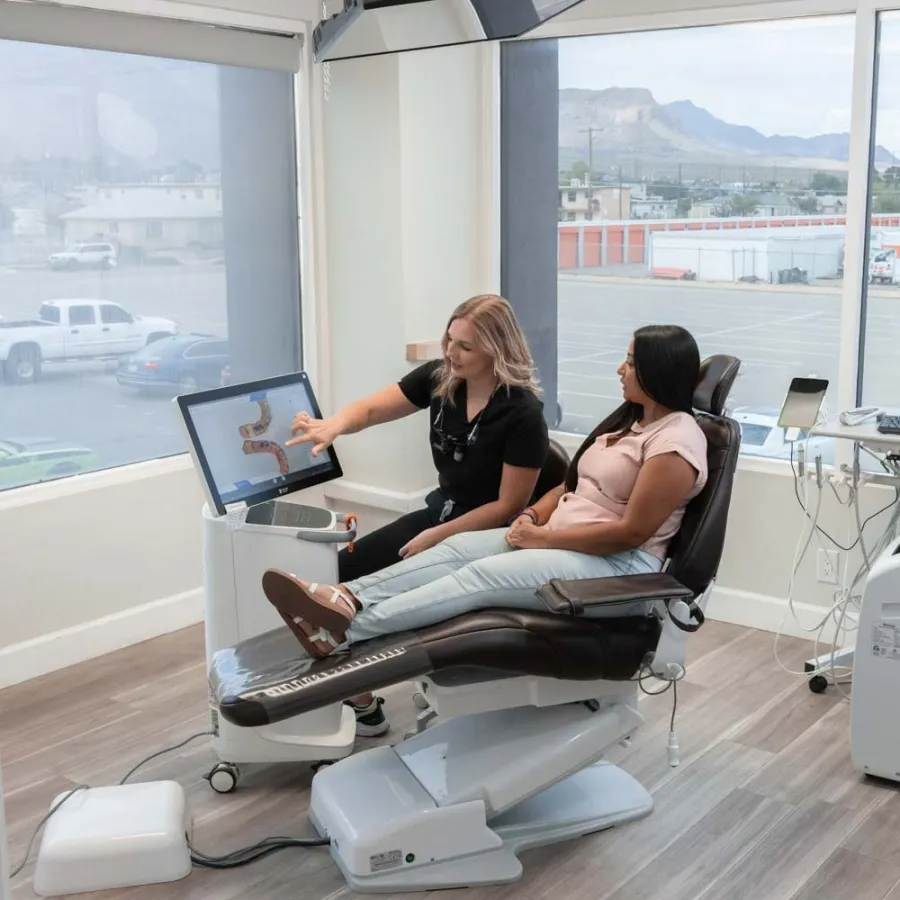 Dentist explaining dental scan results on screen to patient seated in dental chair in modern clinic.