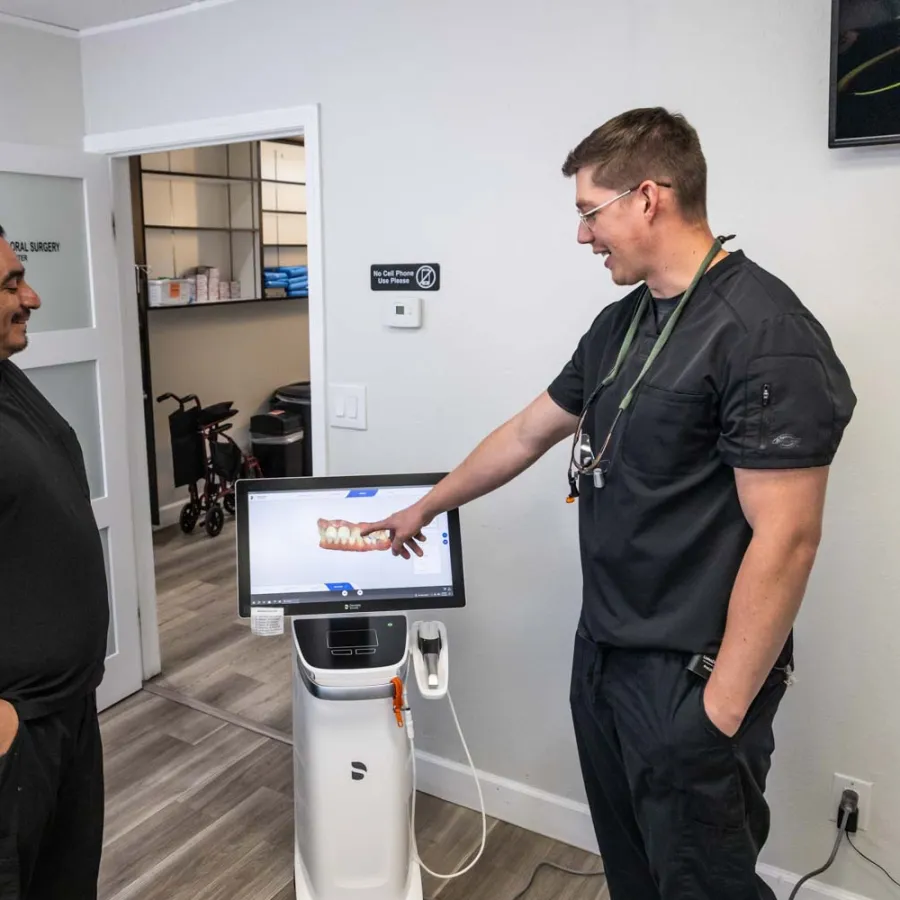 Two dental professionals in black scrubs discuss 3D dental imaging displayed on a screen in a clinic room.