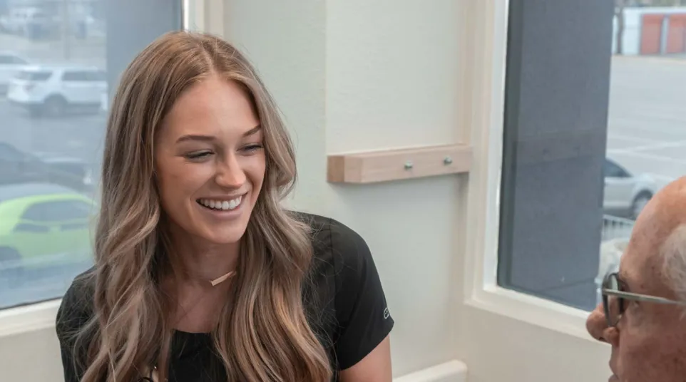 Smiling female dental professional discusses dental model with older male patient in clinic room.