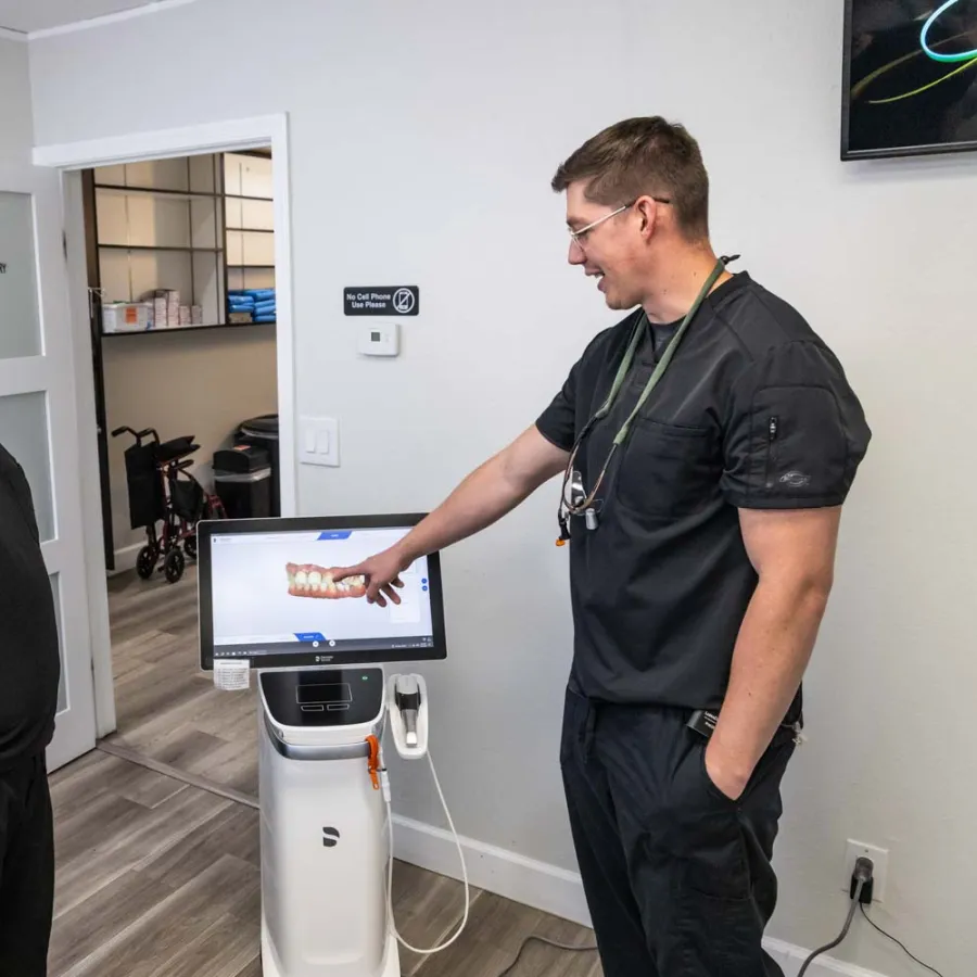 Two dental professionals in black scrubs discuss 3D dental imaging displayed on a screen in a clinic room.