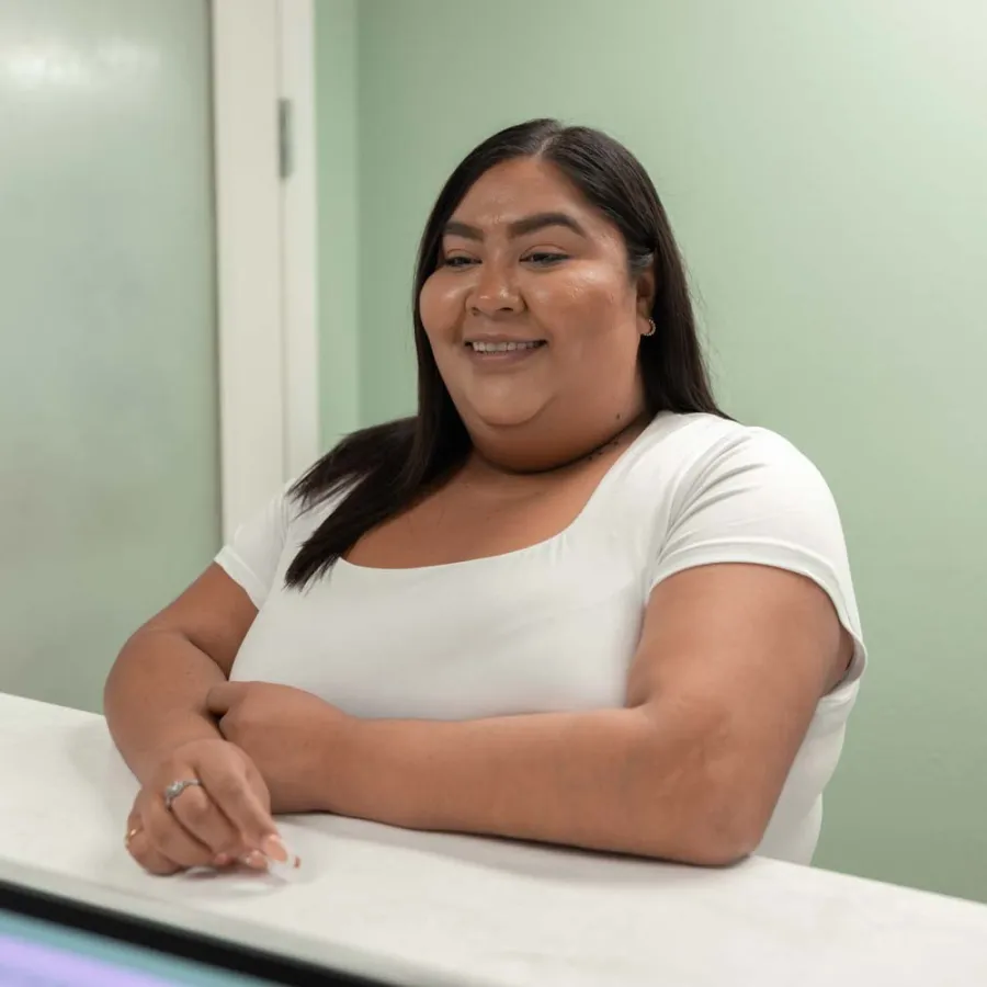 Smiling woman in white shirt sitting at reception desk with mint green walls and frosted glass door behind her
