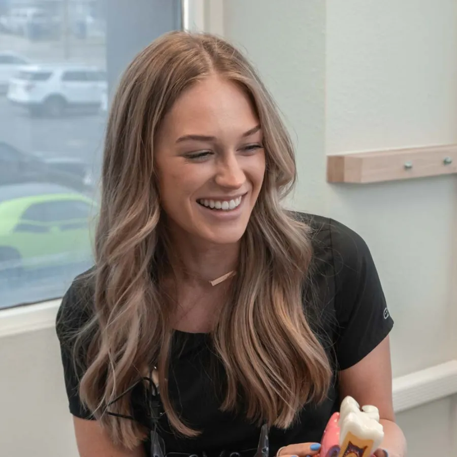 Smiling female dental professional discusses dental model with older male patient in clinic room.